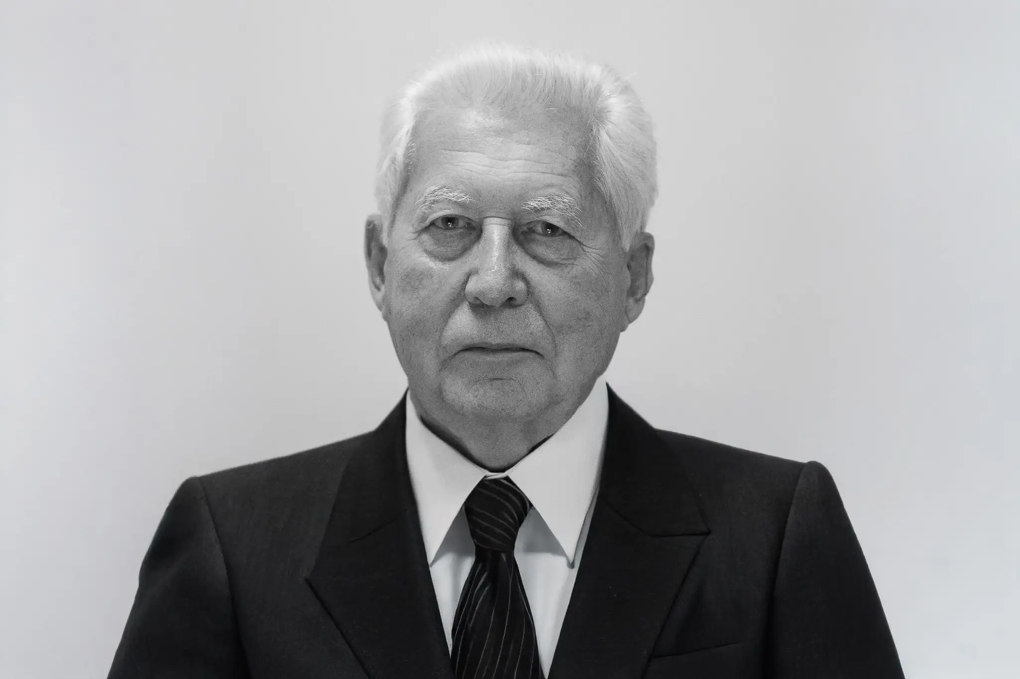 Czarno-biały portret starszego mężczyzny w garniturze i krawacie, na neutralnym tle.